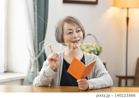 リビングで年金手帳を見るシニア女性 リビングで年金手帳を見るシニア女性 140223866