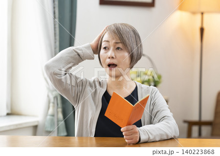 リビングで年金手帳を見るシニア女性 リビングで年金手帳を見るシニア女性 140223868