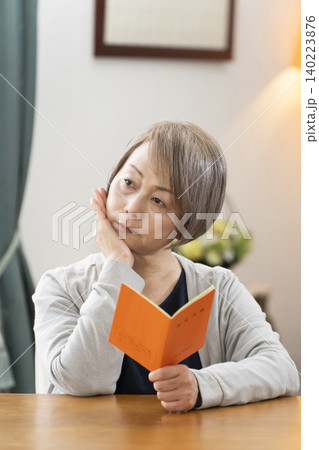 リビングで年金手帳を見るシニア女性 リビングで年金手帳を見るシニア女性 140223876
