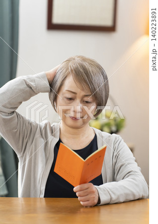 リビングで年金手帳を見るシニア女性 リビングで年金手帳を見るシニア女性 140223891