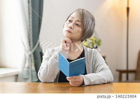 リビングで年金手帳を見るシニア女性 リビングで年金手帳を見るシニア女性 140223904