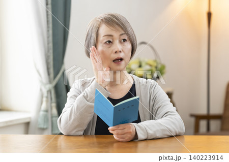 リビングで年金手帳を見るシニア女性 リビングで年金手帳を見るシニア女性 140223914
