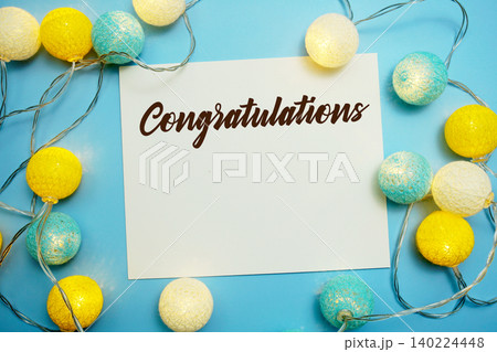 Congratulations text written on paper card with LED cotton balls decorations on blue background Congratulations text written on paper card with LED cotton balls decorations on blue background 140224448