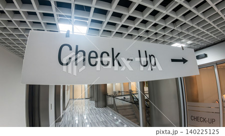 Hanging Check-Up directional sign with a right arrow in a bright, modern hospital interior corridor. Preventive medicine and healthcare wayfinding. 140225125