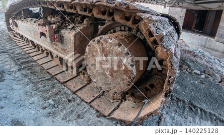 Close-up of heavy machinery rusty metal tracks and drive sprocket on a muddy construction site. Concept of industrial power, earthmoving, and heavy equipment. Close-up of heavy machinery rusty metal tracks and drive sprocket on a muddy construction site. Concept of industrial power, earthmoving, and heavy equipment. 140225128