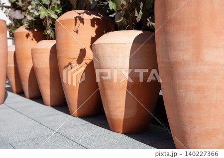 Row of large terracotta clay pots creating a rhythmic perspective in daylight. Decorative Mediterranean style clay planters standing in a line outside. Close up of ceramic flowerpots with sharp Row of large terracotta clay pots creating a rhythmic perspective in daylight. Decorative Mediterranean style clay planters standing in a line outside. Close up of ceramic flowerpots with sharp 140227366