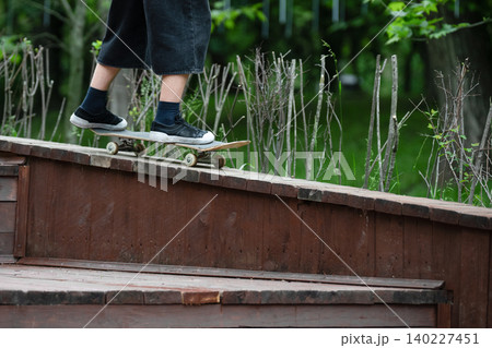 Low angle view of a person on a skateboard riding on a wooden ramp in a park.  Close-up of skateboarder feet in sneakers balancing on a board at an outdoor skatepark. 140227451