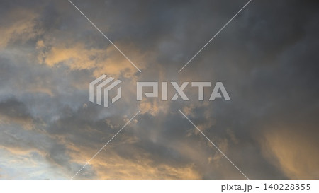 Wide scenic view captures dense smoky dark storm cloud layers at dawn. Soft golden orange sunrise light illuminates misty sky details, creating a beautiful dramatic natural backdrop template. 140228355