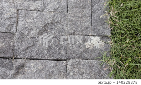 Top view captures rough textured grey stone pavers placed beside green grass. Natural rock materials border the lawn edge, creating a nice textured background template for landscape design. 140228878