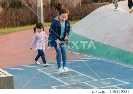 Two active Asian sisters or friends playing outdoor games on a colorful playground path, focus on movement and healthy childhood development through physical activity and social interaction. 140229522