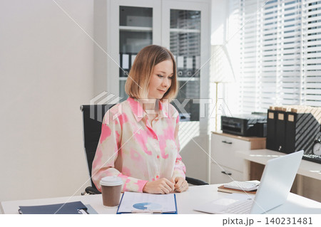 Confident and Composed: A professional businesswoman exudes confidence and composure as she works on her laptop, surrounded by the vibrant energy of a modern office space. Confident and Composed: A professional businesswoman exudes confidence and composure as she works on her laptop, surrounded by the vibrant energy of a modern office space. 140231481