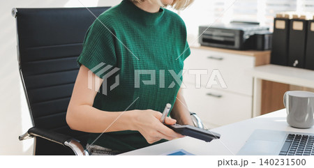 Concept of business working, Businesswoman sitting while writing and checking business analytic document report and holding tablet with computer pc, smartphone on desk in her workstation. Concept of business working, Businesswoman sitting while writing and checking business analytic document report and holding tablet with computer pc, smartphone on desk in her workstation. 140231500