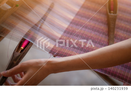 Woman working on weaving machine for weave handmade fabric. Textile weaving. Weaving using traditional hand weaving loom on cotton strands. Textile or cloth production in Thailand. Asian culture. Woman working on weaving machine for weave handmade fabric. Textile weaving. Weaving using traditional hand weaving loom on cotton strands. Textile or cloth production in Thailand. Asian culture. 140231939