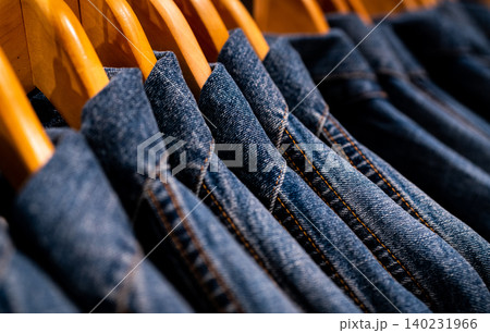 Selective focus on jacket jeans hanging on rack in clothes shop. Denim jeans with jeans pattern. Textile industry. Jeans fashion and shopping concept. Clothing concept. Denim jacket on rack for sale. Selective focus on jacket jeans hanging on rack in clothes shop. Denim jeans with jeans pattern. Textile industry. Jeans fashion and shopping concept. Clothing concept. Denim jacket on rack for sale. 140231966