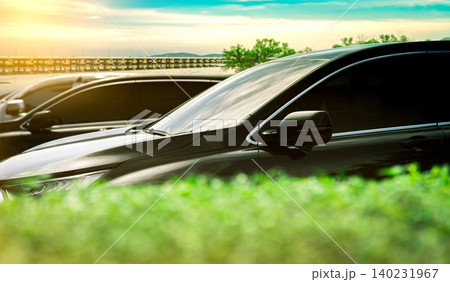 Luxury black shiny SUV Car parked on concrete parking area by the sea with blue sky, clouds, mountain and concrete bridge. Car stock for sale. Car parking lot. Automotive Industry. Road trip travel. Luxury black shiny SUV Car parked on concrete parking area by the sea with blue sky, clouds, mountain and concrete bridge. Car stock for sale. Car parking lot. Automotive Industry. Road trip travel. 140231967