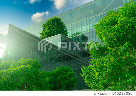 Eco-friendly building with vertical garden in modern city. Green tree forest on sustainable glass building. Energy-saving architecture with vertical garden. Office building with green environment. 140232050