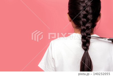 Back view of Asian woman with braided hairstyle is cutting with scissors for donate to cancer patients. Hair donation for breast cancer person. Woman with black long hair braid on pink background. Back view of Asian woman with braided hairstyle is cutting with scissors for donate to cancer patients. Hair donation for breast cancer person. Woman with black long hair braid on pink background. 140232055