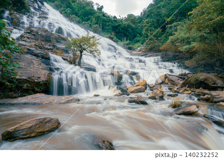 Beautiful waterfall with a lush green forest in the background. The water is flowing down the rocks and creating a beautiful scene. Sustainable waterfall in lush forest promoting water sustainability. Beautiful waterfall with a lush green forest in the background. The water is flowing down the rocks and creating a beautiful scene. Sustainable waterfall in lush forest promoting water sustainability. 140232252