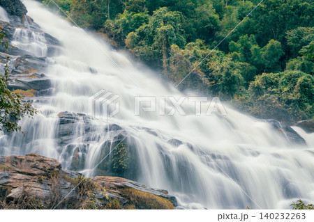 Beautiful waterfall with a lush green forest in the background. The water is flowing down the rocks and creating a beautiful scene. Sustainable waterfall in lush forest promoting water sustainability. 140232263