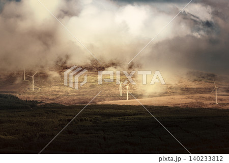 A wide shot shows turbines on a hillside, seen through a layer of fog and above dark trees. A wide shot shows turbines on a hillside, seen through a layer of fog and above dark trees. 140233812