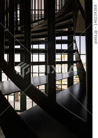 a dark iron spiral staircase creates a striking rhythm of shadow and steel against a daylight-flooded gridded window. The composition balances deep foreground silhouettes with a bright, airy 140234369