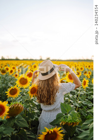 Woman poses in sunflower field in a dress and hat. Enjoy the moment. Active lifestyle. Woman poses in sunflower field in a dress and hat. Enjoy the moment. Active lifestyle. 140234554