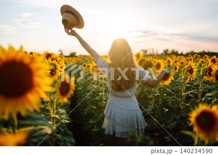 Woman poses in sunflower field in a dress and hat. Enjoy the moment. Active lifestyle. Woman poses in sunflower field in a dress and hat. Enjoy the moment. Active lifestyle. 140234590