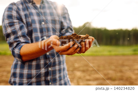 Farmer's hands take the soil from field and check its quality. Experienced male hands hold the soil. 140234820