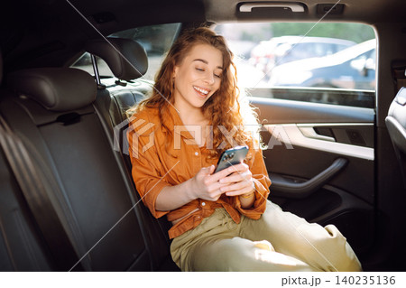 A young woman with a smartphone chats in the back seat of a car. Transport concept. Lifestyle. 140235136