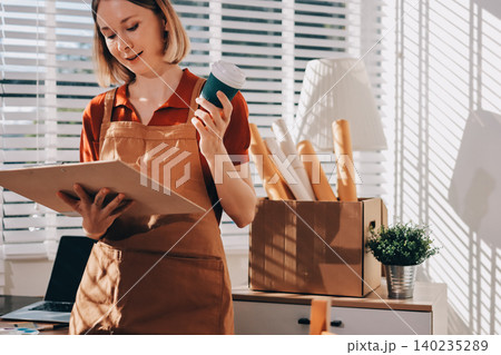 Picture of serious concentrated young Caucasian female artist sitting at desk with painting accessories, holding tube of oil paint, mixing colors on palette; unfinished painting on canvas near her Picture of serious concentrated young Caucasian female artist sitting at desk with painting accessories, holding tube of oil paint, mixing colors on palette; unfinished painting on canvas near her 140235289