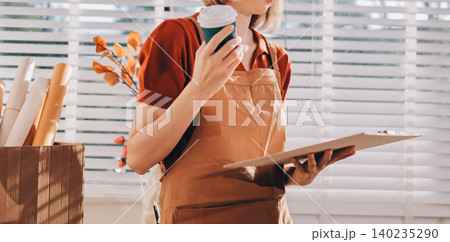 Picture of serious concentrated young Caucasian female artist sitting at desk with painting accessories, holding tube of oil paint, mixing colors on palette; unfinished painting on canvas near her Picture of serious concentrated young Caucasian female artist sitting at desk with painting accessories, holding tube of oil paint, mixing colors on palette; unfinished painting on canvas near her 140235290