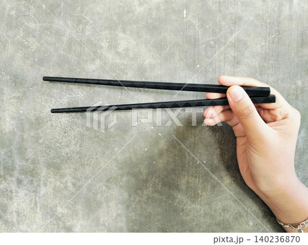 Hand Holding Black Chopsticks on Concrete Wall Background Hand Holding Black Chopsticks on Concrete Wall Background 140236870