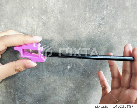 Hand Holding Pencil and Sharpener on Concrete Wall Background Hand Holding Pencil and Sharpener on Concrete Wall Background 140236887