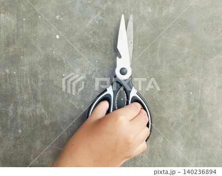 Hand Holding Scissors Against Grey Concrete Wall Background Hand Holding Scissors Against Grey Concrete Wall Background 140236894