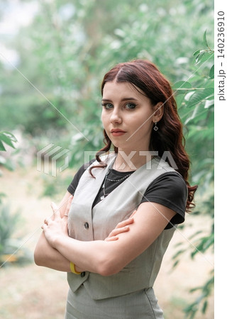 girl with crossed arms stands against a background of greenery girl with crossed arms stands against a background of greenery 140236910