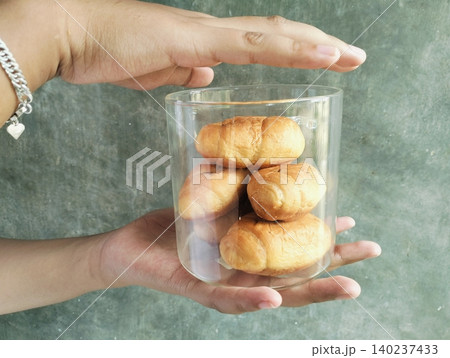 Hand Holding Croissant in a Glass Jar on Concrete Wall Background Hand Holding Croissant in a Glass Jar on Concrete Wall Background 140237433