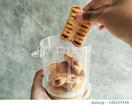 Hand Holding Jam Filled Pastry and Glass Cookie Jar on Concrete Background Hand Holding Jam Filled Pastry and Glass Cookie Jar on Concrete Background 140237439