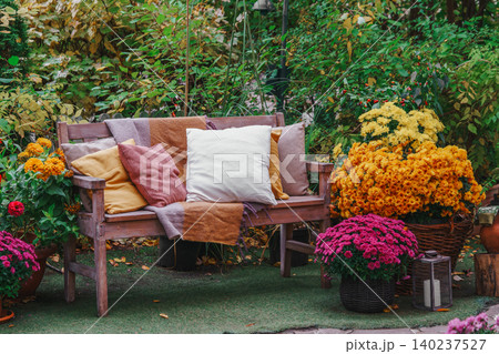 Wooden garden bench with pillows among autumn flowers and colorful foliage in fall backyard Wooden garden bench with pillows among autumn flowers and colorful foliage in fall backyard 140237527