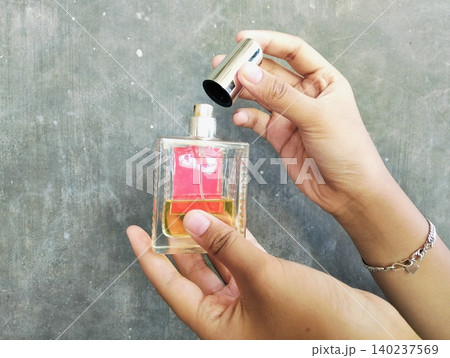 Hand Holding a Perfume Bottle on Concrete Wall Background 140237569