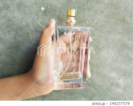 Hand Holding an Empty Perfume Bottle on Concrete Wall Background 140237579