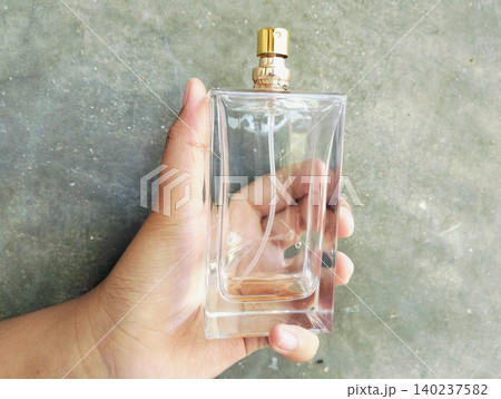 Hand Holding an Empty Perfume Bottle on Concrete Wall Background 140237582