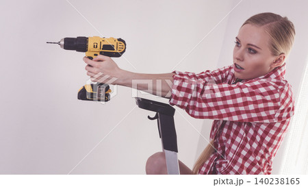 Woman using drill on ladder Woman using drill on ladder 140238165