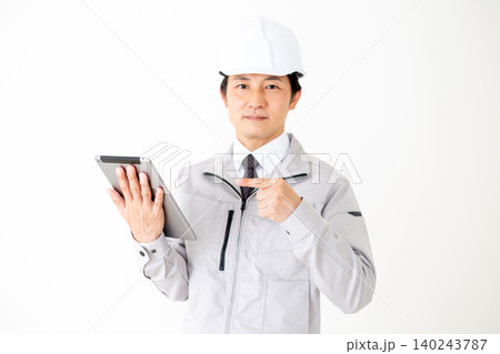 タブレットを指差すヘルメットをかぶったグレーの作業着のミドル男性ビジネスマン白バック タブレットを指差すヘルメットをかぶったグレーの作業着のミドル男性ビジネスマン白バック 140243787