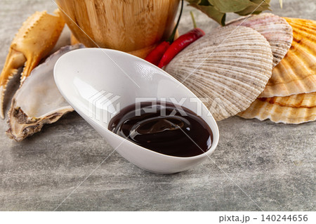 Dark seafood sauce in white bowl with shells and crab claw 140244656