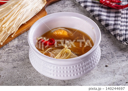 Hot noodle soup with enoki mushrooms, chili peppers, and tofu in white bowl on rustic table Hot noodle soup with enoki mushrooms, chili peppers, and tofu in white bowl on rustic table 140244697