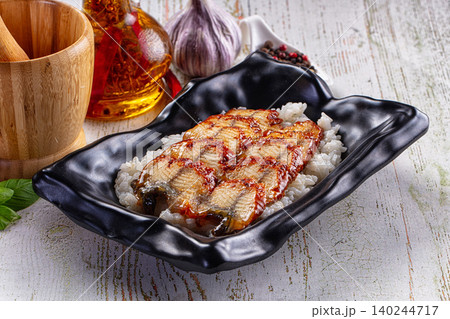 Grilled eel unagi served on white rice in black ceramic bowl with garlic and oil Grilled eel unagi served on white rice in black ceramic bowl with garlic and oil 140244717