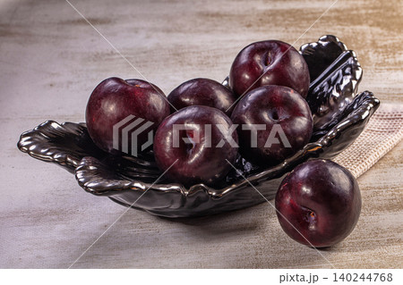 Ripe red plums in elegant black bowl on textured surface Ripe red plums in elegant black bowl on textured surface 140244768