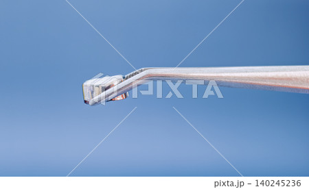 Macro of medical tweezers holding an artificial dental crown on a blue background with copy space. Macro of medical tweezers holding an artificial dental crown on a blue background with copy space. 140245236