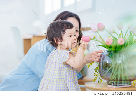 花瓶の花に触れる乳幼児の女の子とお母さん 花瓶の花に触れる乳幼児の女の子とお母さん 140250481