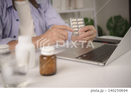 Close up senior hands holding medicine blister pack and pointing at capsule while using laptop. Elderly patient checking prescription, side effects or ordering drugs online via telemedicine service. 140250694